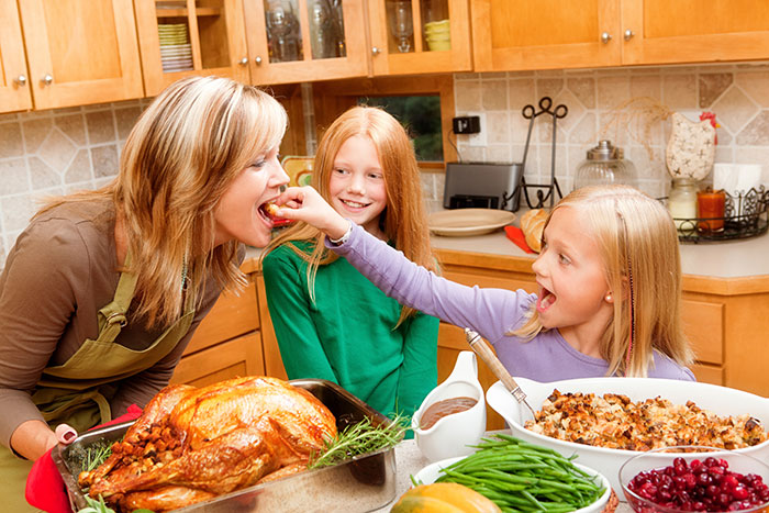 mother and two daughters with thanksgiving feast in kitchen daughter feeding mother