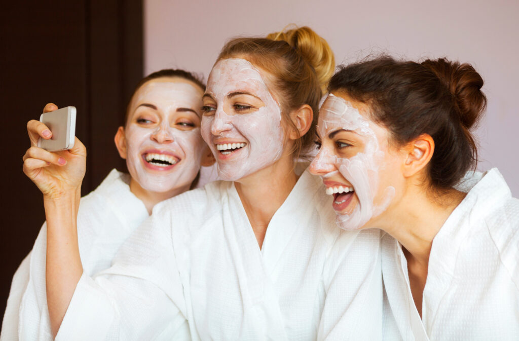Three young happy women with face masks taking selfi at spa resort. Friendship and wellbeing concept